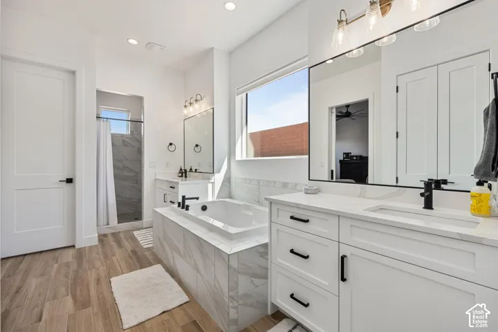 Primary Bathroom featuring dual white vanities with quartz countertops, undermount sinks, matte black fixtures, tile-surround soaking tub, and wood-finish flooring