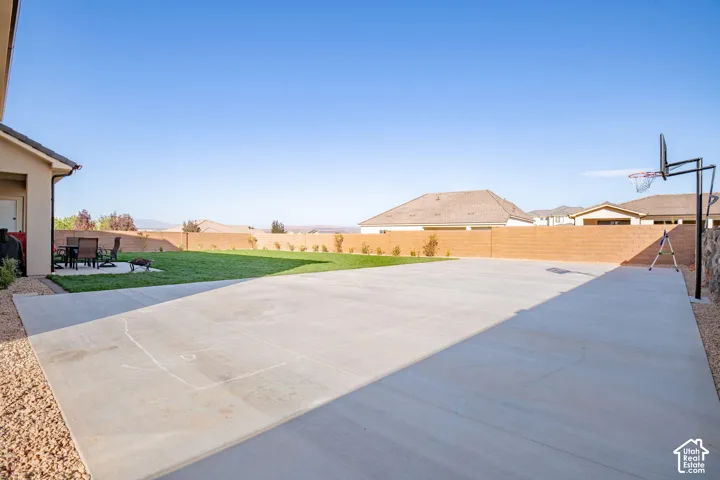 Expansive backyard featuring a large concrete patio, a manicured lawn, a masonry perimeter wall, and a fixed basketball standard