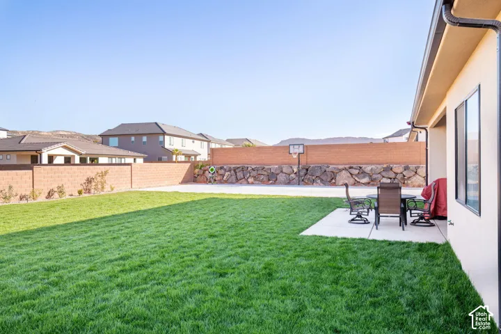 Backyard featuring a manicured lawn, concrete patio, perimeter masonry wall, and stacked-stone retaining wall