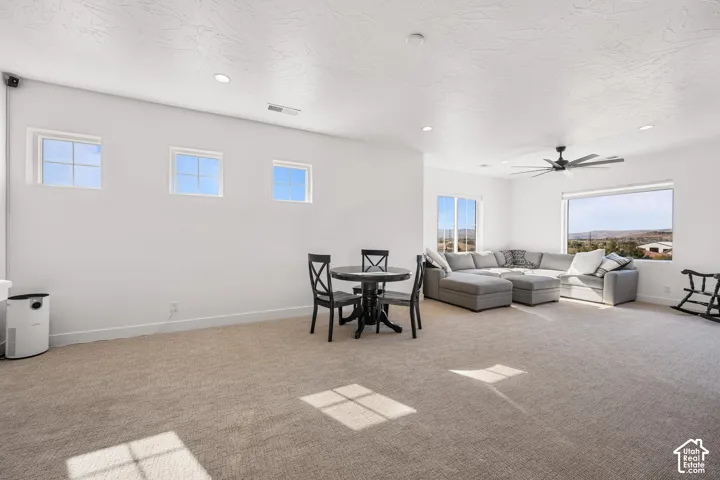 Open-concept space featuring neutral carpeting, recessed lighting, a modern ceiling fan, and large windows with mountain scenery