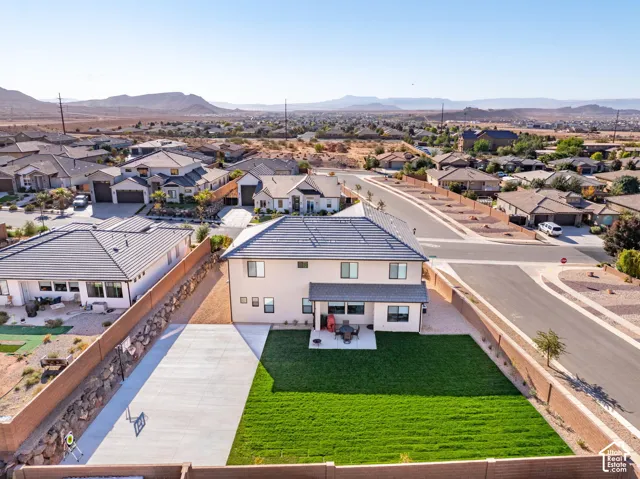 Two-story residence featuring a tile roof, an expansive rear lawn, a concrete patio, a stone retaining wall, and a multi-car paved side apron