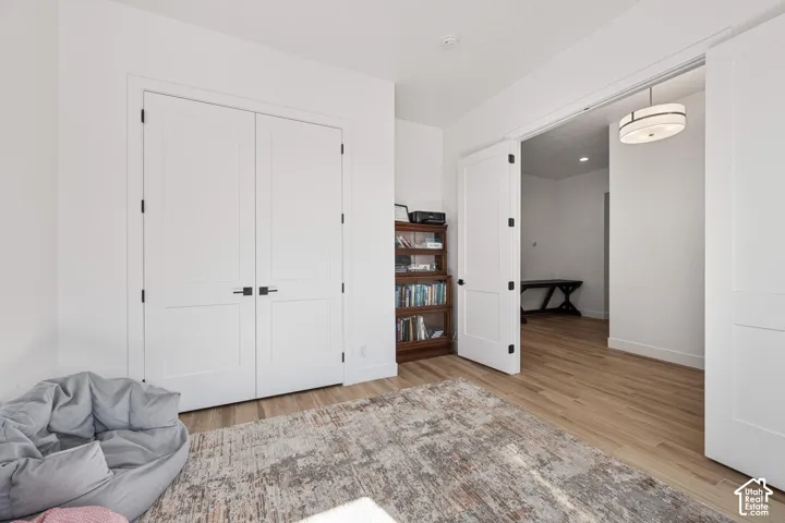 Flex bed/office Wood-finish flooring, white shaker-style double doors with matte black hardware, and a contemporary drum pendant light fixture
