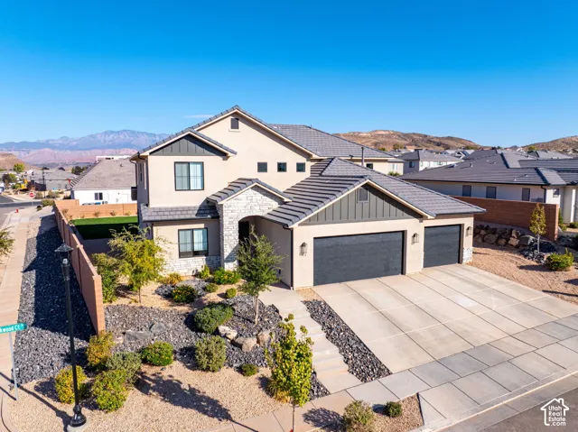 Two-story stucco and stone exterior featuring a tile roof, board-and-batten siding accents, and an attached three-car garage set against a mountain backdrop