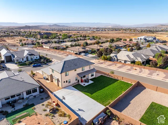 Aerial perspective of a two-story residence featuring a tile roof, a concrete driveway, a rear concrete patio, and a fenced backyard with a lawn
