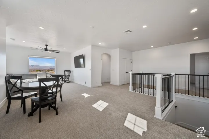 Open floor plan featuring recessed lighting, a modern ceiling fan, neutral carpeting, and a staircase with a white balustrade and black metal spindles