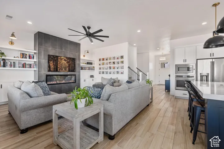 Linear gas fireplace with floor-to-ceiling tile surround, wood-finish flooring, built-in shelving, recessed lighting, and stainless steel wall-mounted oven