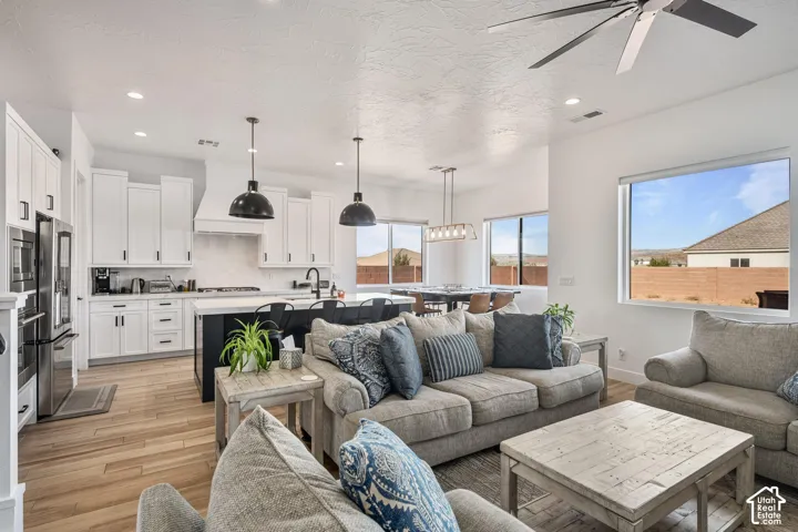 Open-concept kitchen featuring white shaker-style cabinetry, a contrasting dark kitchen island with a light-toned countertop, wood-finish flooring, matte black pendant lighting, and recessed ceiling lighting