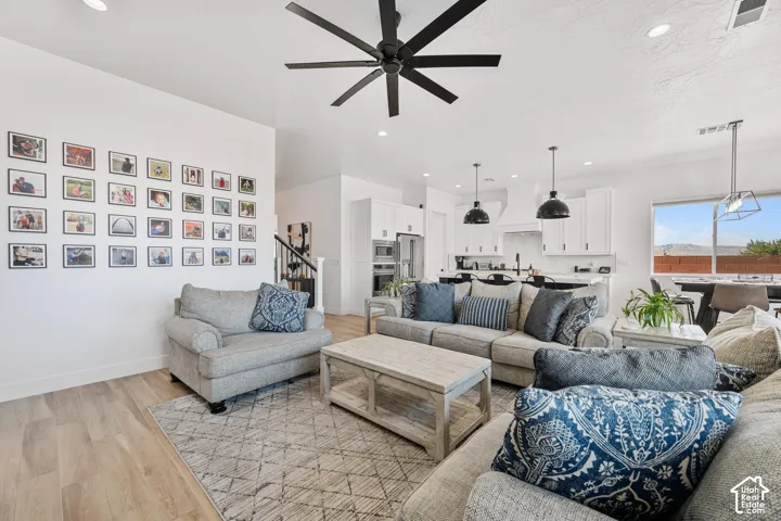 Open-concept interior featuring light wood-finish flooring, a contemporary matte black ceiling fan, recessed lighting, and a kitchen equipped with white cabinetry and integrated stainless steel appliances
