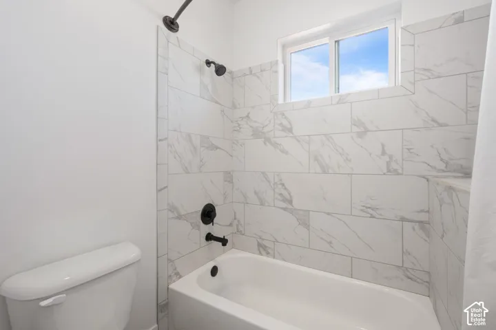 Bathroom featuring a white porcelain tub, matte black shower and tub fixtures, and floor-to-ceiling large-format stone-patterned wall tile