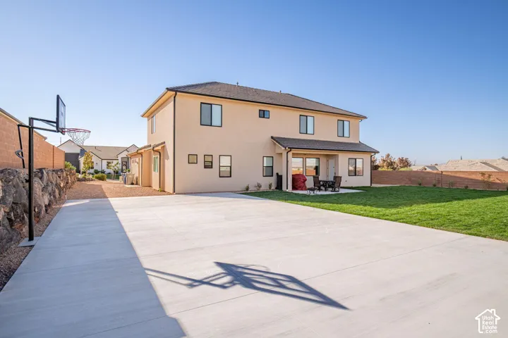 Two-story stucco exterior featuring a large concrete patio, manicured lawn, stone retaining wall, and an integrated basketball standard