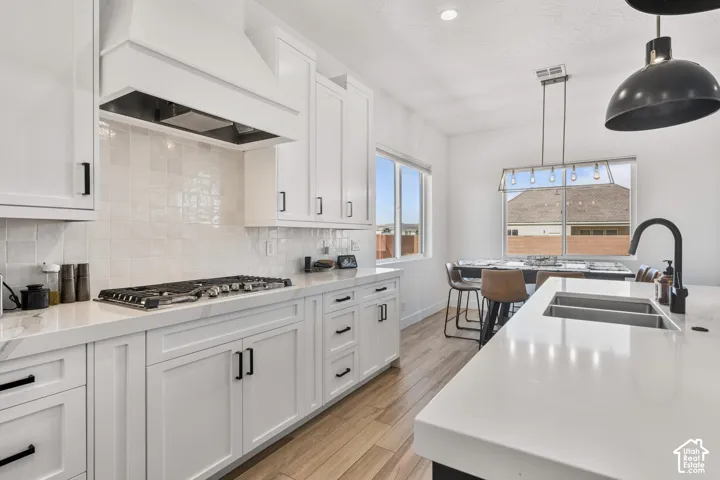 Kitchen featuring white cabinetry, quartz countertops, a tiled backsplash, wood-finish flooring, and a center island with a dual-basin sink