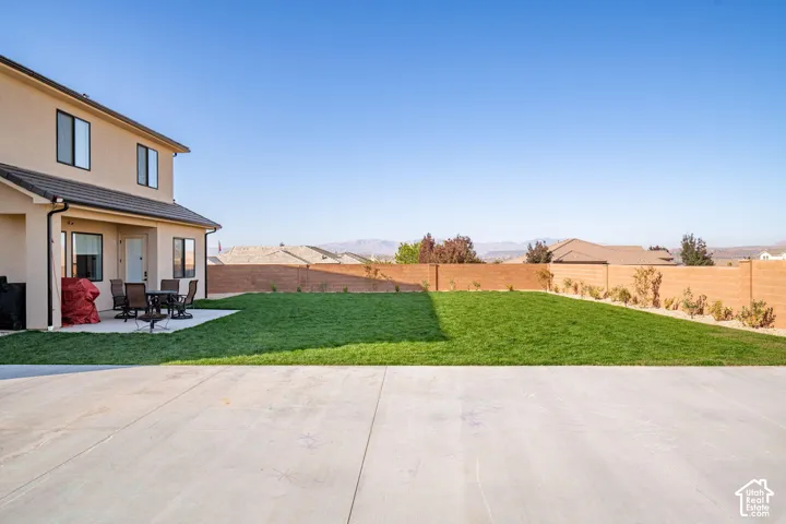 Expansive backyard featuring a manicured lawn, concrete patio, masonry privacy wall, and desert mountain backdrop