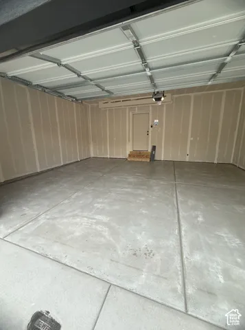 Two-car garage featuring a smooth concrete floor, unfinished drywall, overhead sectional door, and an elevated entry door with wood-frame steps