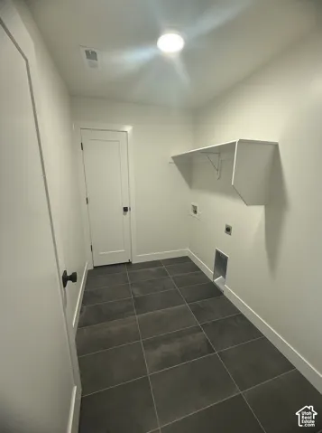 Utility room featuring large-format grey tile flooring, a wall-mounted shelving unit, and a single-panel interior door with matte black hardware
