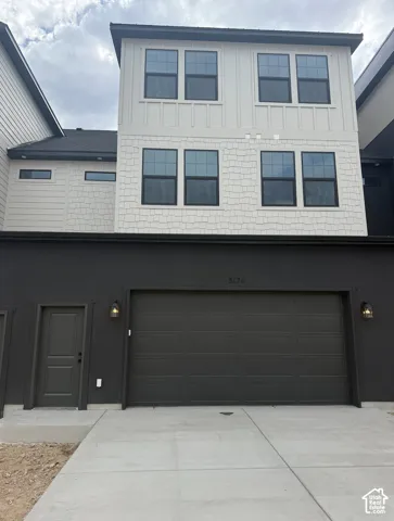 Multi-level exterior featuring a combination of white board-and-batten and shake siding, dark-toned smooth stucco lower level, integrated two-car garage, and exterior wall-mounted lighting