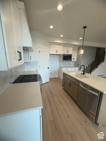 Kitchen featuring wood-finish flooring, white cabinetry with matte black hardware, quartz countertops, a central island with an undermount sink, and recessed lighting