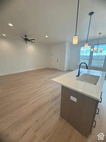 Kitchen island featuring a white stone countertop, undermount sink, and matte black faucet, complemented by wood-finish cabinetry, wood-finish flooring, recessed lighting, and pendant lighting