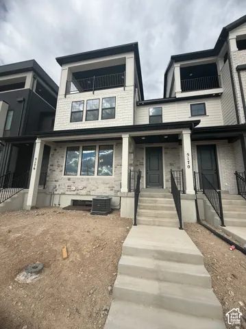 Modern multi-level exterior featuring light stone veneer, horizontal siding, black metal balcony railings, and a covered front entry