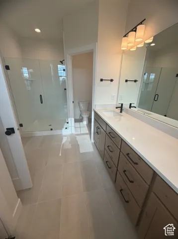 Bathroom featuring a dual-sink vanity with light wood-finish cabinetry, quartz countertops, matte black hardware, and a walk-in glass-enclosed shower with tile flooring