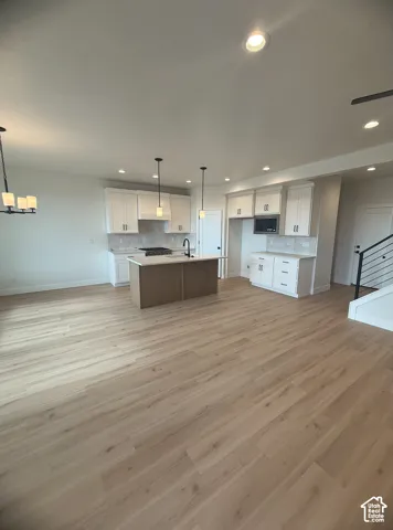 Kitchen featuring white shaker-style cabinetry, wood-finish kitchen island, recessed lighting, wood-finish flooring, and a metal stair railing