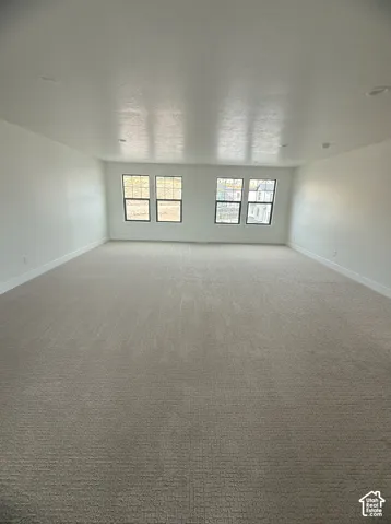 Neutral-toned carpeting, recessed ceiling lighting, and expansive wall space accented by four grid-style windows with black frames
