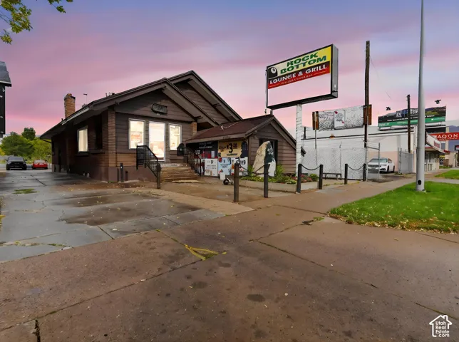 Commercial property featuring a shingled roof, exterior wood siding, masonry chimney, paved parking area, and an elevated signage structure