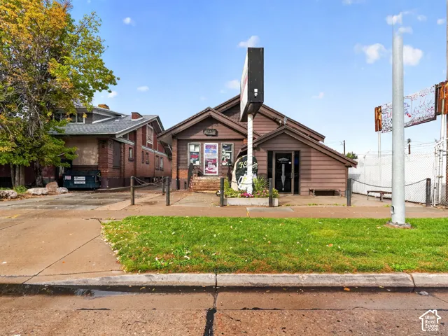 Commercial structure with wood siding, gable rooflines, exterior sign post, and paved exterior area