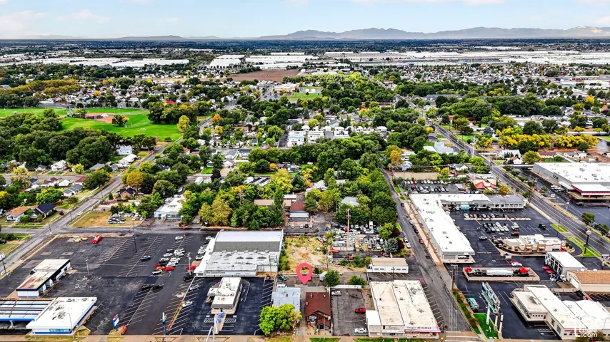 Aerial view of a commercial site featuring paved parking areas, mature tree canopy coverage, and mountain range backdrop