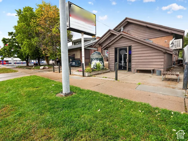 Exterior building featuring brown horizontal lap siding, a concrete walkway, a built-in elevated planter, and a dedicated signage pole