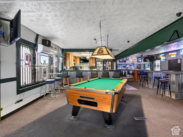 Spacious recreation area featuring a built-in bar with corrugated metal siding, textured ceiling, wall-mounted ductless climate control unit, and window security bars