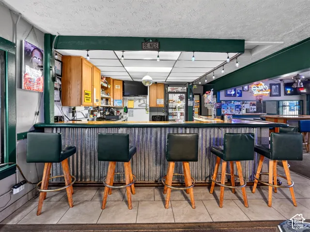 Custom bar featuring a corrugated metal front, wood-finish cabinetry, drop ceiling with integrated lighting, and tile flooring