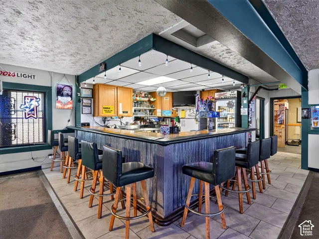 Custom bar area featuring dark wood-finish cabinetry, a textured corrugated metal front, a dark countertop, integrated pendant lighting, and ceramic tile flooring