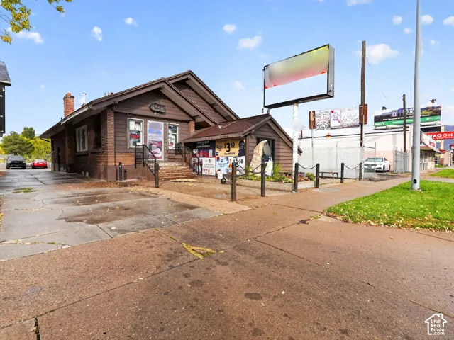 Exterior featuring a brick and wood-sided structure, shingled roofing, an elevated entryway with metal railing, and an integrated signage post