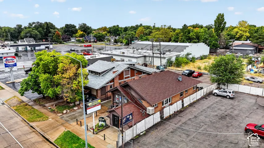Commercial property featuring a brick and wood-sided exterior, a multi-pitched roofline, mature trees, and a paved parking area enclosed by a privacy fence