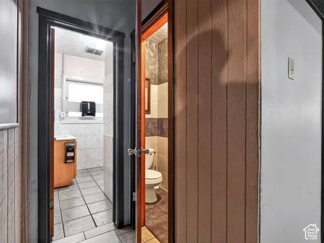 Wood-paneled wall surfacing, tile flooring, and bathroom featuring a vanity cabinet with stone-surfaced countertop and wall-mounted tile finishes