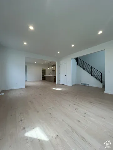 Open-concept interior featuring wood-finish flooring, recessed lighting, a staircase with a horizontal metal railing, and a kitchen island with pendant lighting