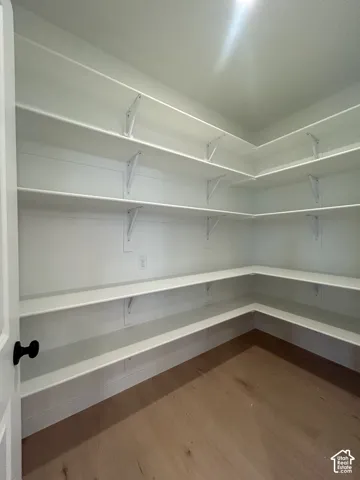 Walk-in storage area featuring multi-level wrap-around shelving, white-finished wall paneling, and wood-finish flooring