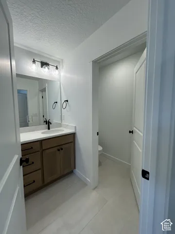 Vanity featuring wood-finish cabinetry, white countertop with integrated basin, matte black hardware, three-light fixture, and ceramic tile flooring