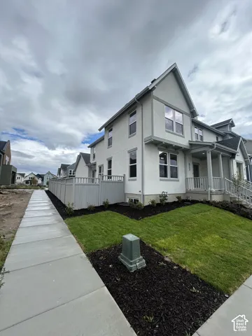 Two-story exterior featuring light-toned stucco siding, dark-trimmed window casings, a covered front porch with railing, and a privacy fence