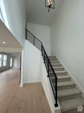 Staircase featuring a matte black horizontal-rail balustrade, carpeted treads, wood-finish flooring, and a geometric pendant light fixture