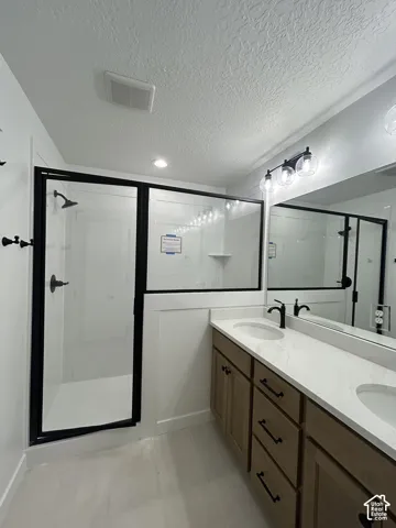 Double vanity featuring wood-finish cabinetry, white stone-composite countertop, matte black hardware, and glass-enclosed shower with black metal framing