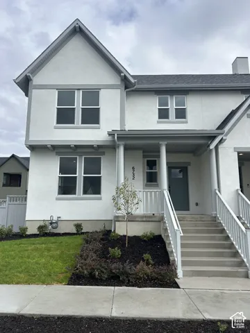 Two-story exterior featuring a light-toned stucco finish, gable roofline, covered front porch with decorative columns, and white picket railing