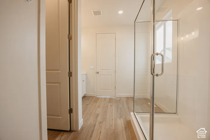 Glass-enclosed shower with a solid-surface surround, wood-finish flooring, and recessed ceiling lighting