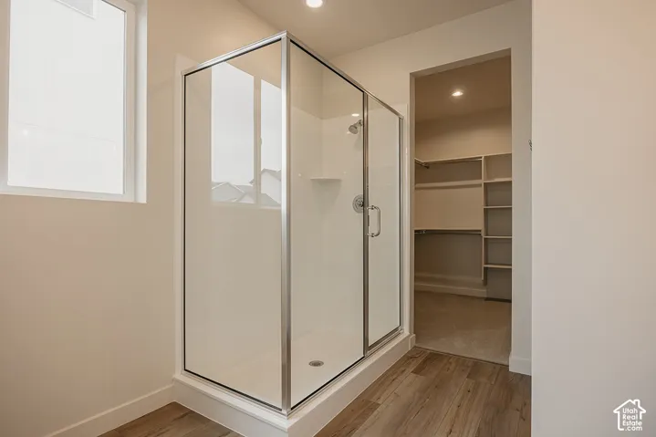 Shower enclosure featuring a chrome frame, glass paneling, and a built-in corner shelf, accented by wood-finish flooring and integrated closet shelving