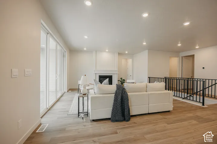 Open-concept living space featuring wood-finish flooring, recessed lighting, floor-to-ceiling sliding glass doors, a fireplace with a decorative mantel, and a black metal railing