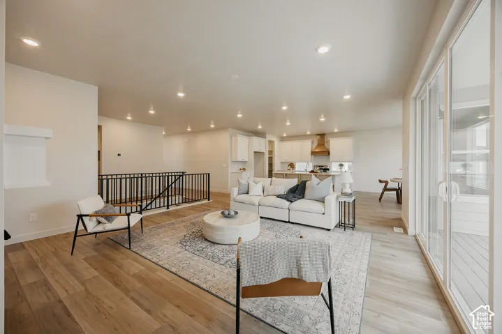Open-concept interior featuring wood-finish flooring, recessed lighting, a modern metal stair railing, and sliding glass doors