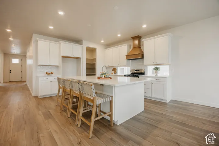 Kitchen featuring white cabinetry, wood-finish flooring, a large center island with a quartz countertop, and a wood-finished range hood