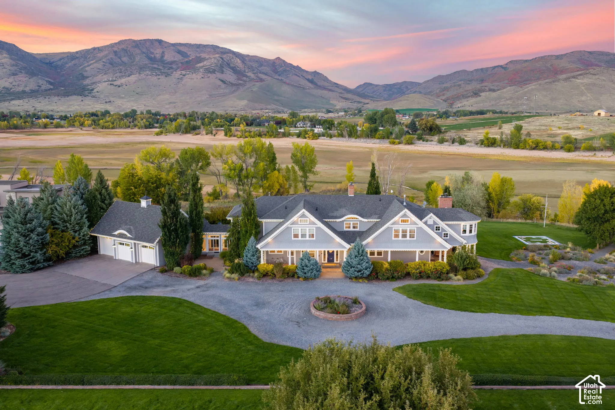 Lakefront residence with neutral siding, expansive manicured grounds, circular gravel driveway, detached garage structure, and prominent mountain backdrop