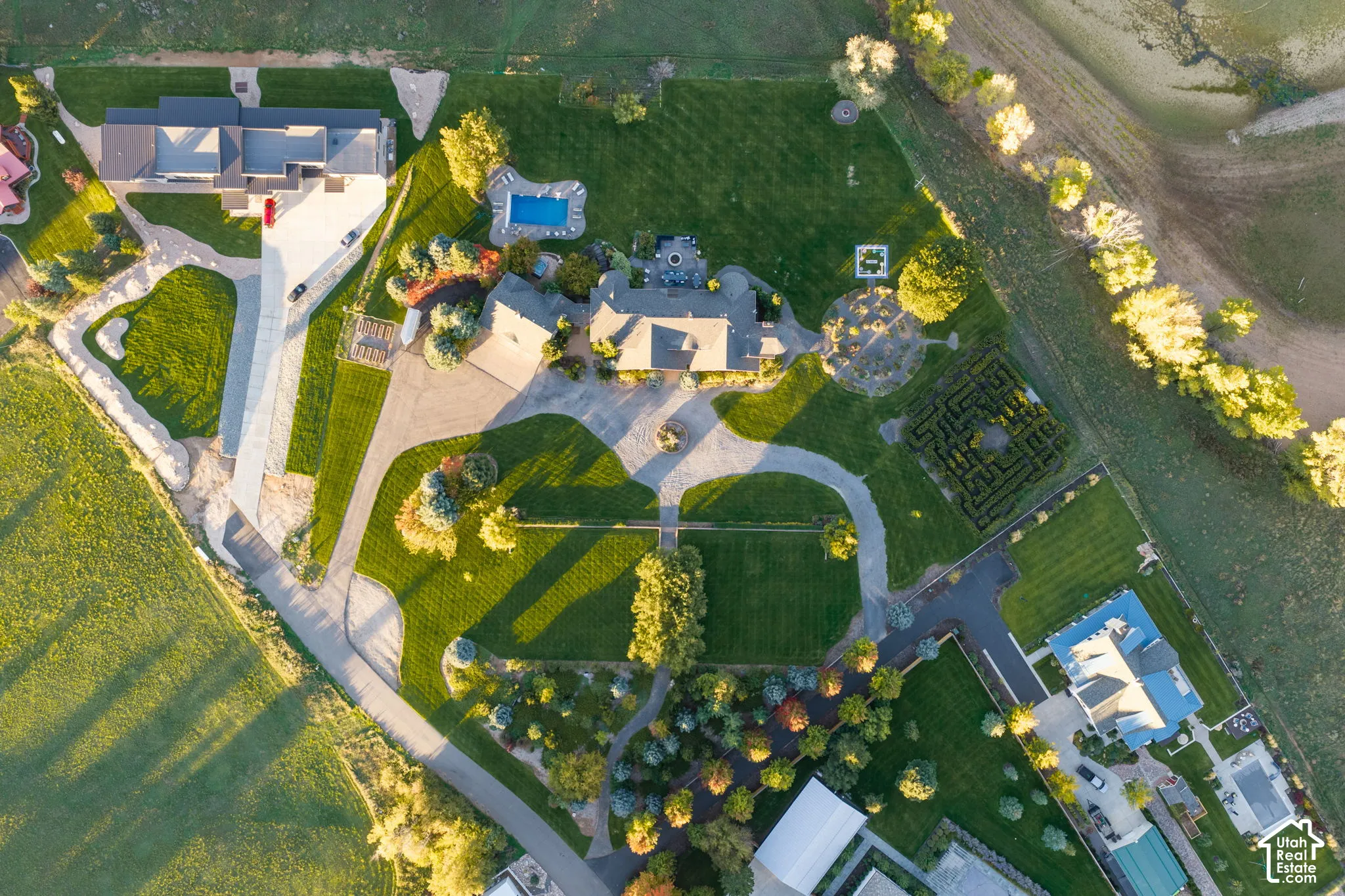 Aerial perspective of expansive grounds featuring an inground swimming pool, a structured hedge maze, mature landscaping, and a circular paved driveway