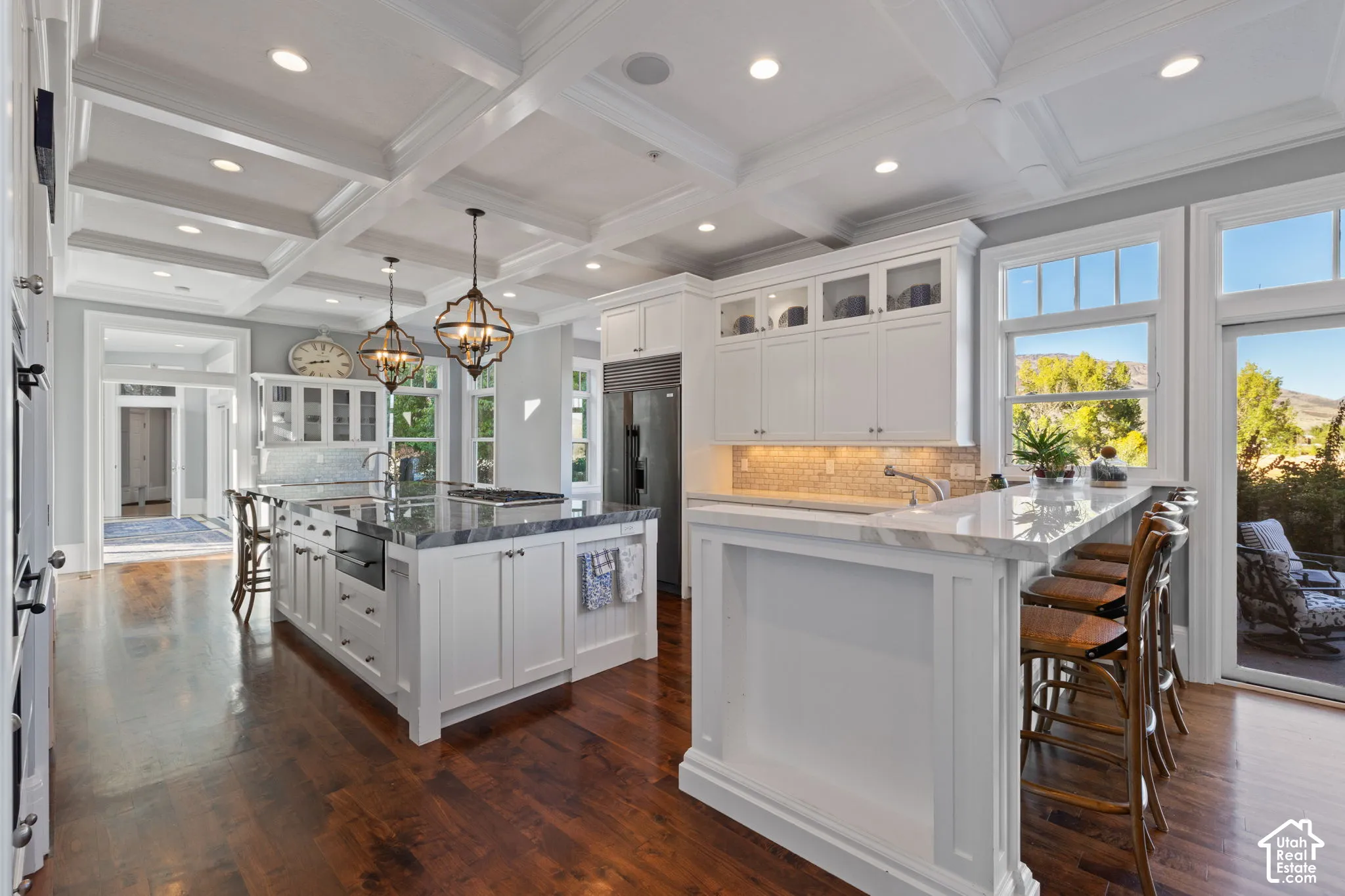 Coffered ceiling, white cabinetry with glass-panel upper doors, stone-topped central island, breakfast bar, and wood-finish flooring